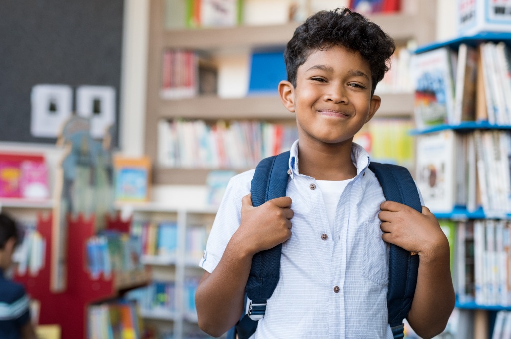 A student with a backpack smiling in a school library